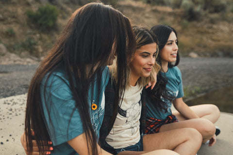 Group of women sitting in front of a small lake/pond. Wearing graphic t-shirts with a steer skull design on the front. PNW style. Wenatchee, WA. Pacific Northwest. Graphic Tee.