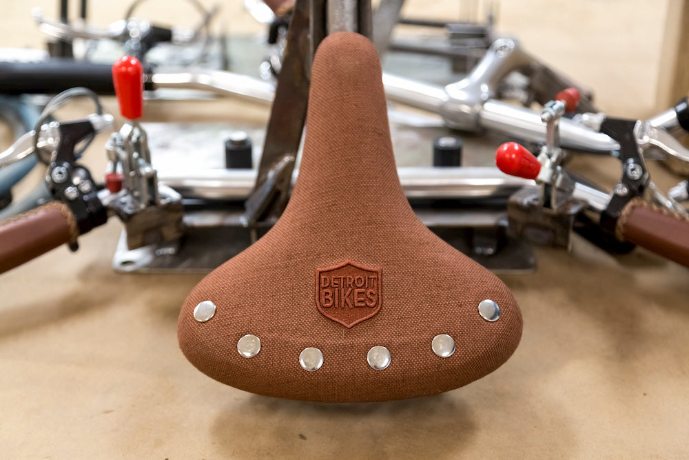 Photo of bicycle parts including a brown bike seat with a Detroit Bikes patch in the foreground.