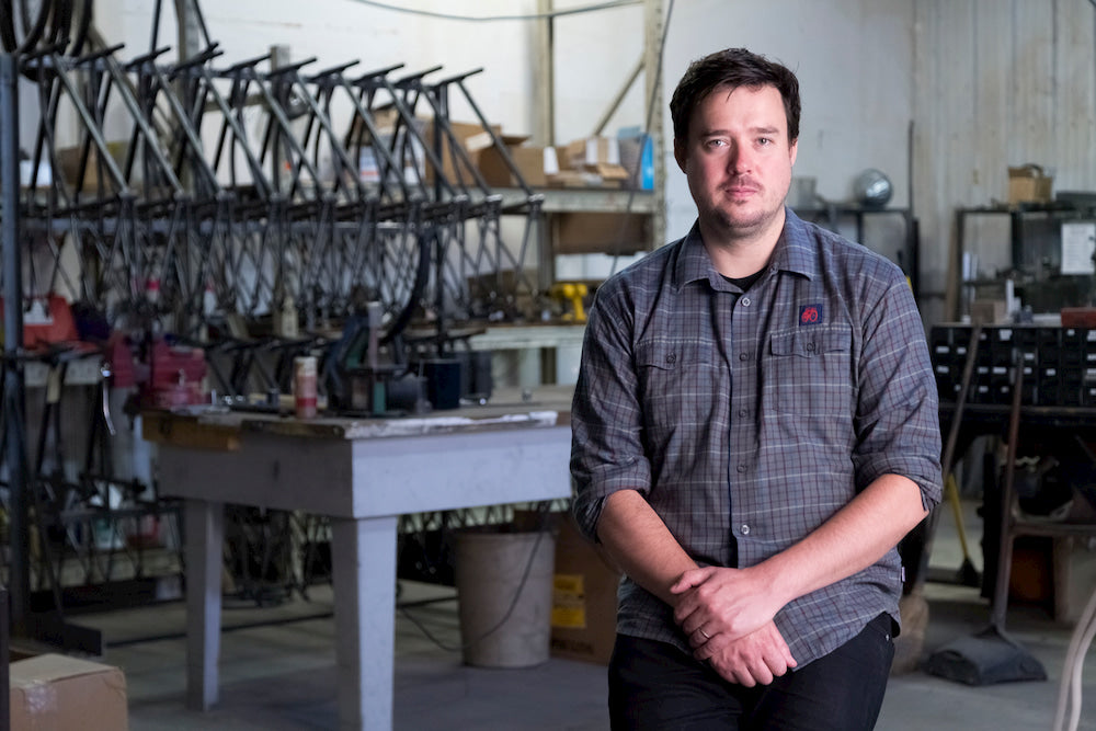 Detroit Bikes founder Zakary Pashak stands in a workshop in his factory. Raw materials and bike frames line the walls.