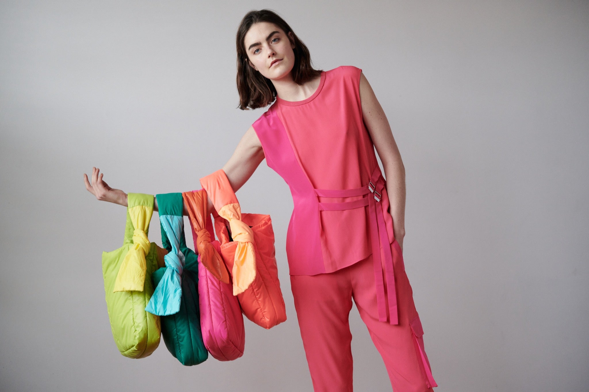 A model in a pink outfit is holding 4 bags created by Caraa. 