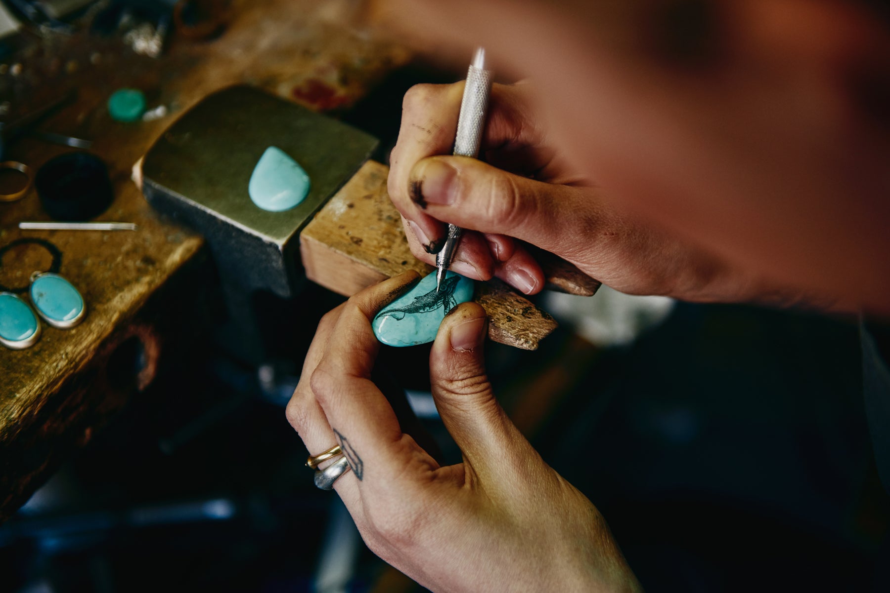 Close up image of jewelry designer Hannah Blount’s hands as she carves an intricate whale illustration into a piece of turquoise.