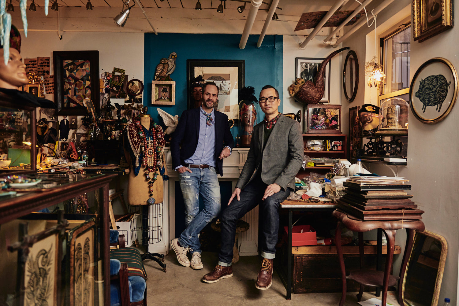 Don Carney and John Ross stand in their eclectic PATCH NYC studio, surrounded by art, jewellery, art supplies, books, and vintage décor.