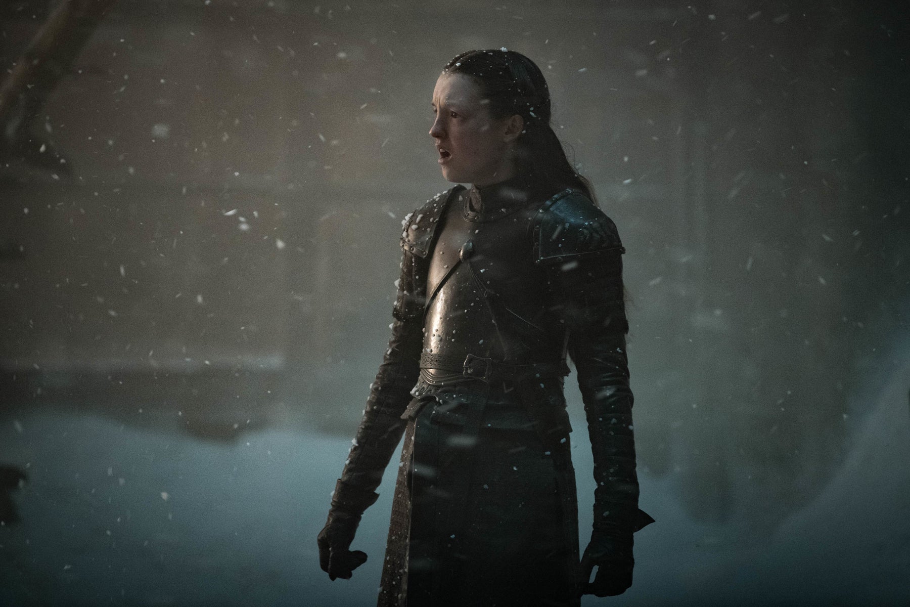 Lyanna Mormont, dressed in armor, stands in the snow and looks off-camera at something approaching.
