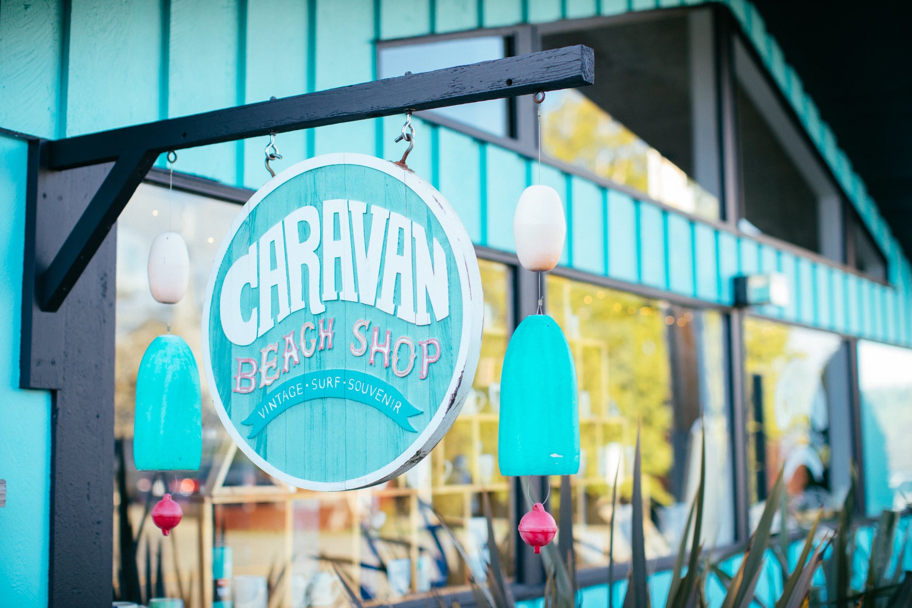 Bright blue wooden sign of Caravan Beach Shop hangs in front of the shop. 