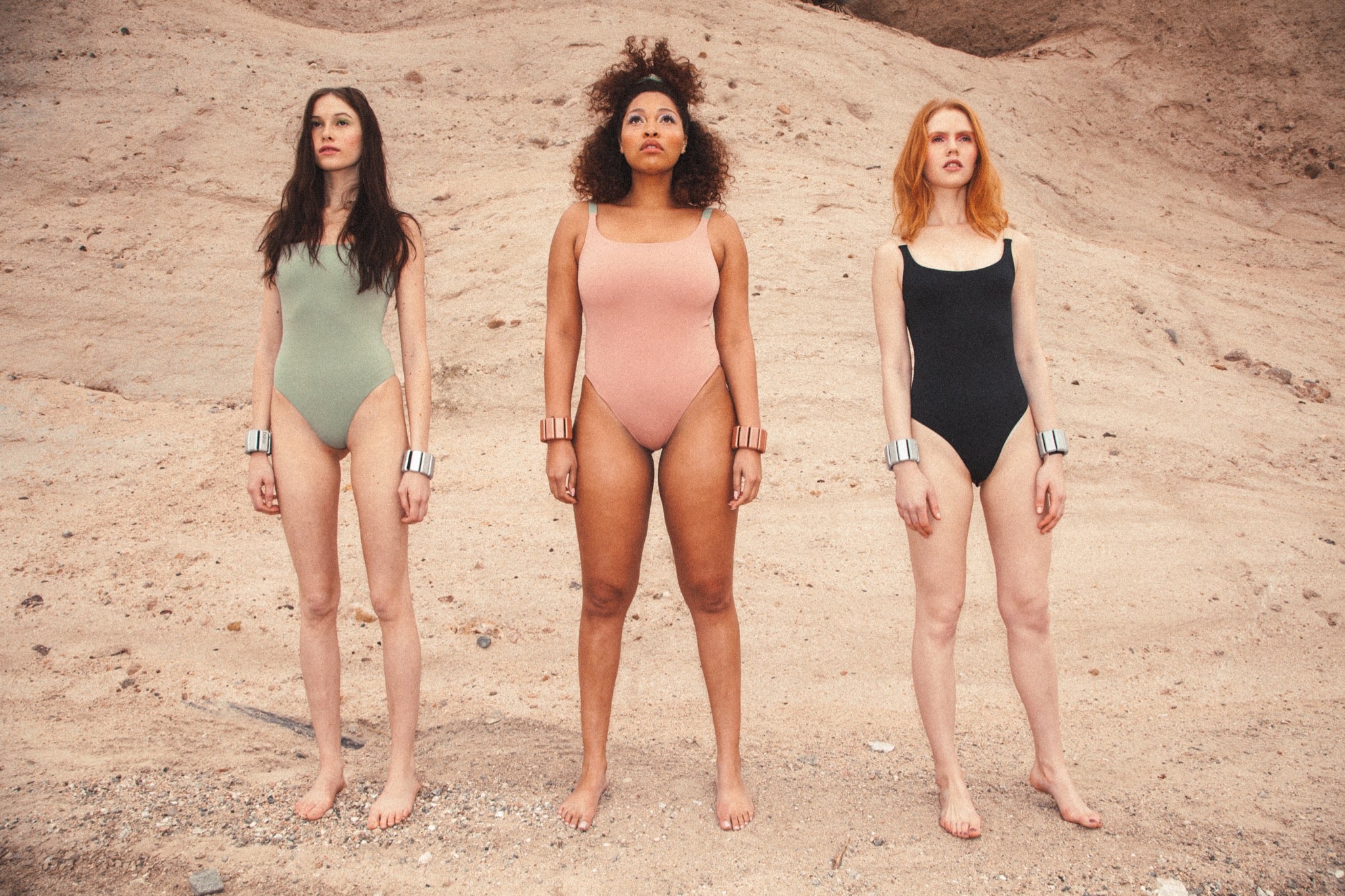 Three models wearing workout bodysuits and Bala Bangles in the desert. 