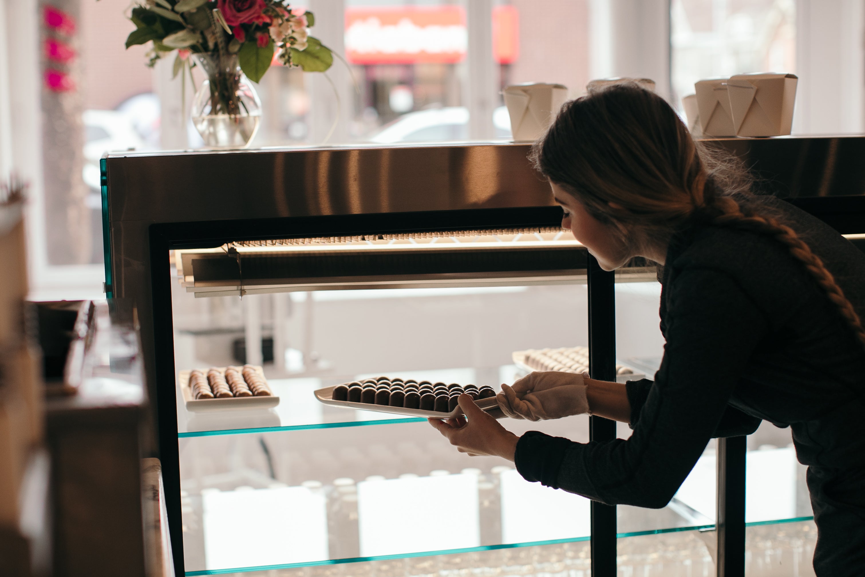 Alicja Buchowicz restocking a glass display with fresh chocolate bonbons. 