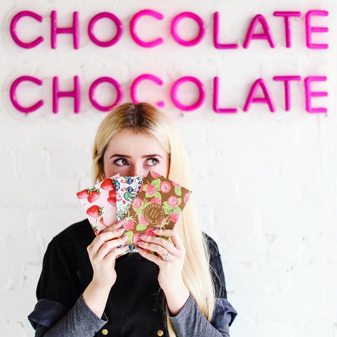 Alicja Buchowicz holding a selection of her postcard chocolate bars within her retail store. 
