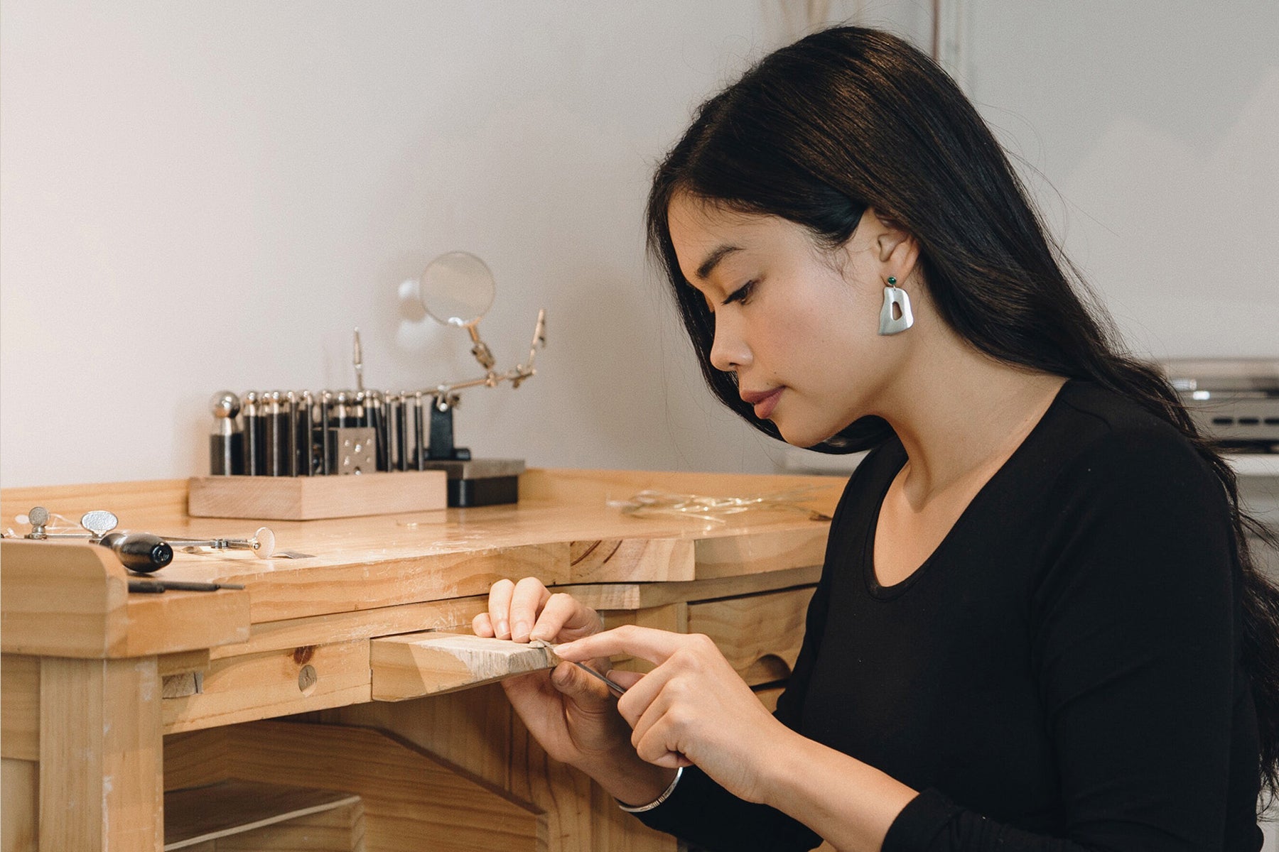 Allison Asis, founder of Cadette Jewelry, at her work bench. She’s wearing a black shirt and refines a piece of jewelry. 