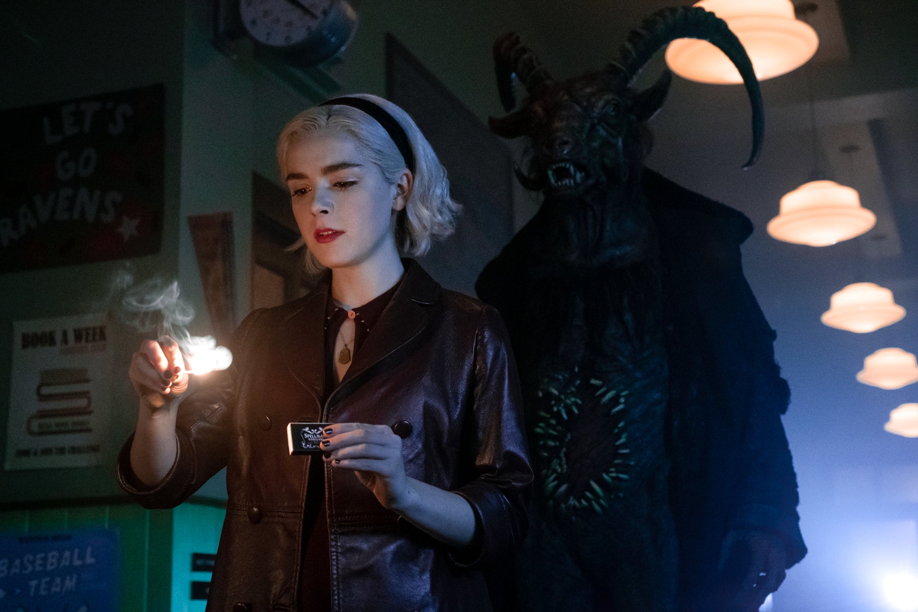 Sabrina Spellman lights a match in a dark hallway while a demon stands behind her in a scene from Chilling Adventures of Sabrina.