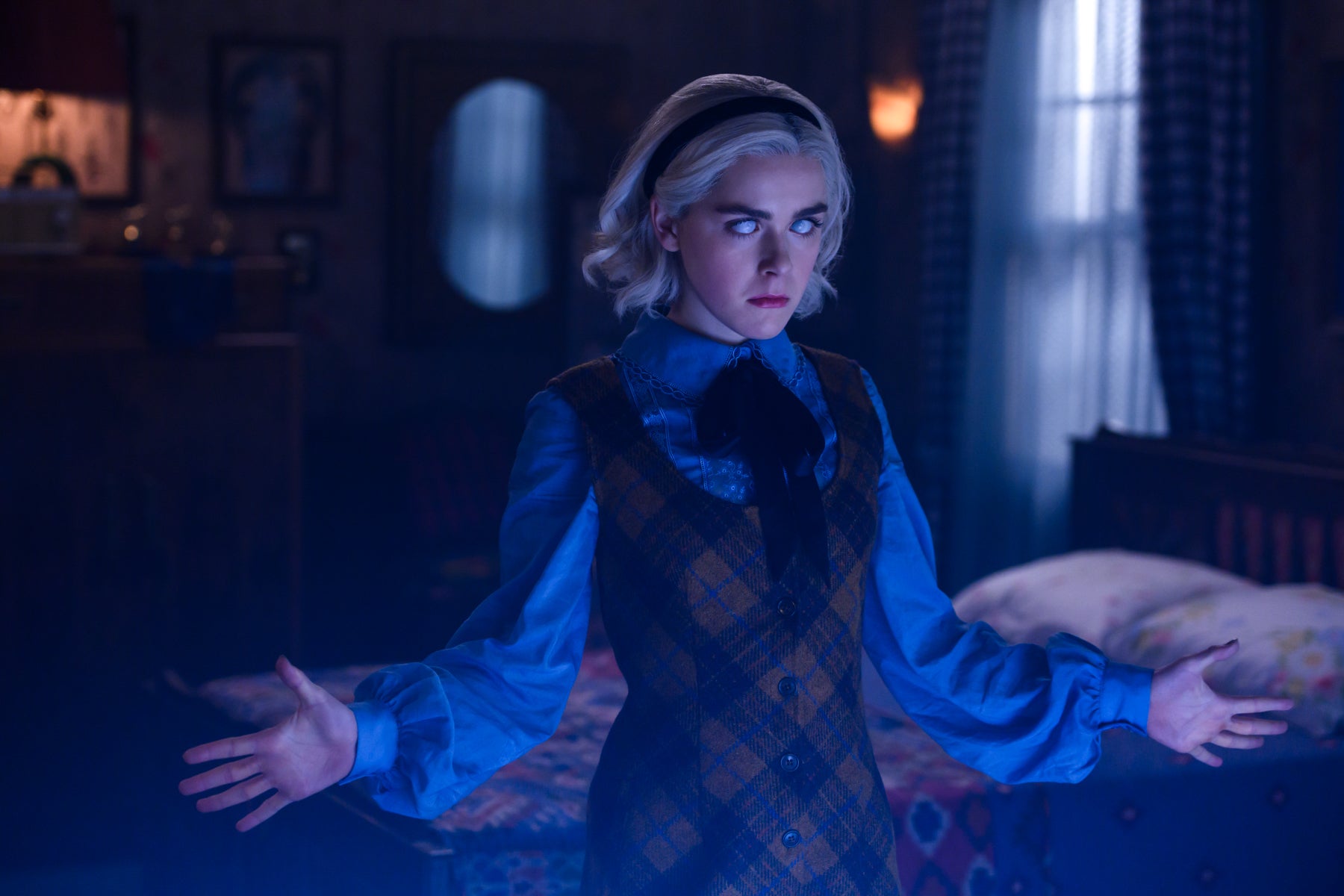 Sabrina Spellman stands with arms outstretched in a darkened room in a scene from Chilling Adventures of Sabrina.