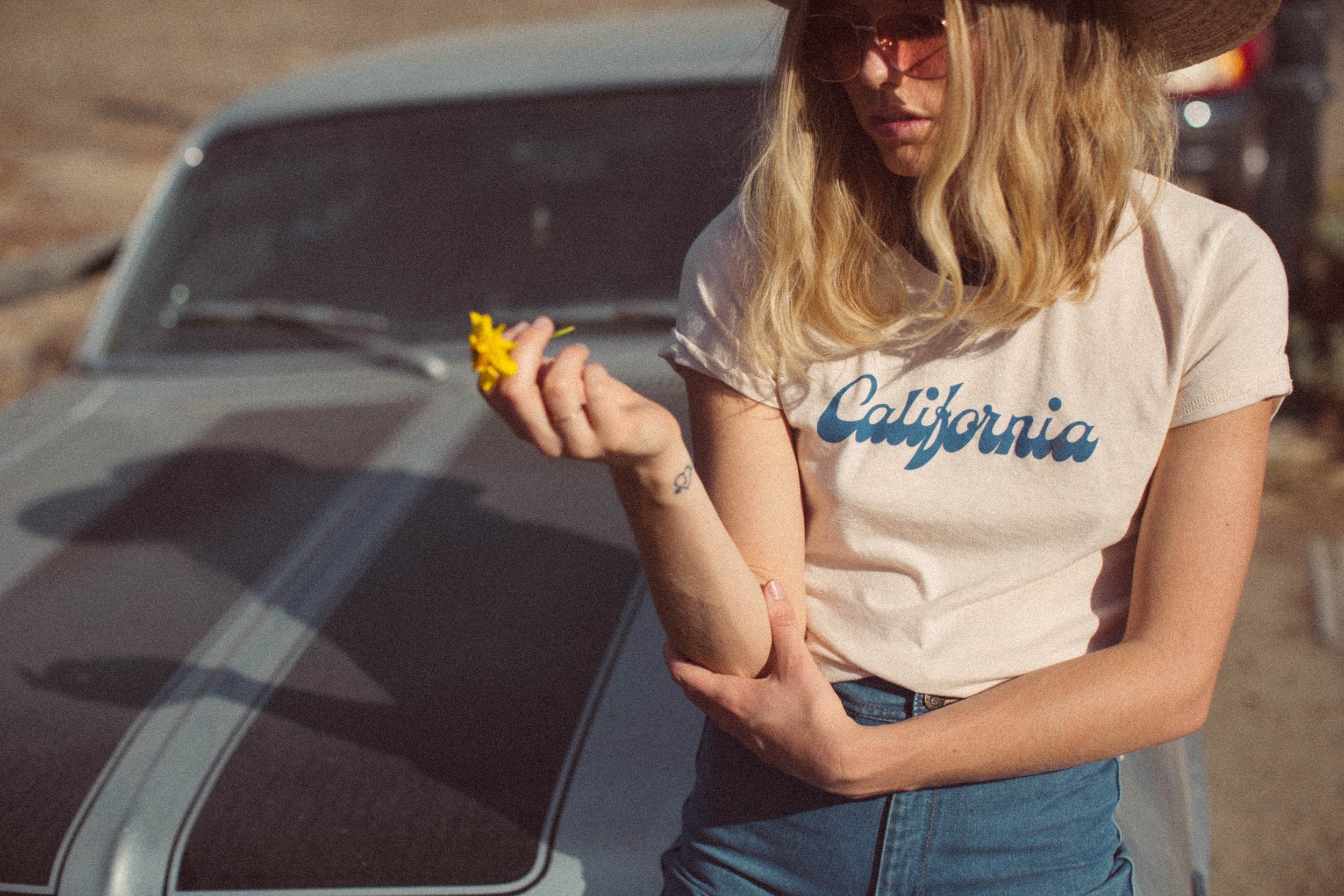 Afbeelding van een model zittend op een auto met een T-shirt aan met daarop de tekst "California"