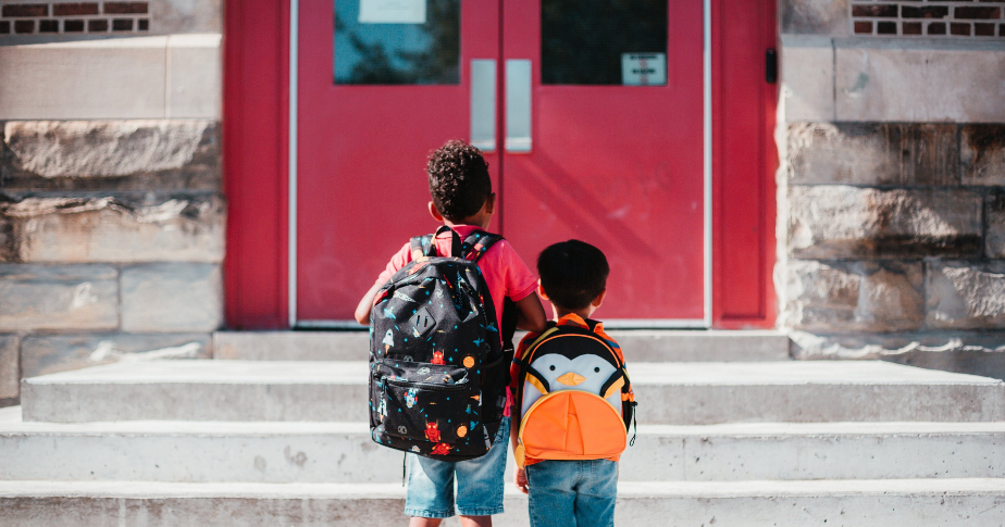 Two students with backpacks heading back into a school.