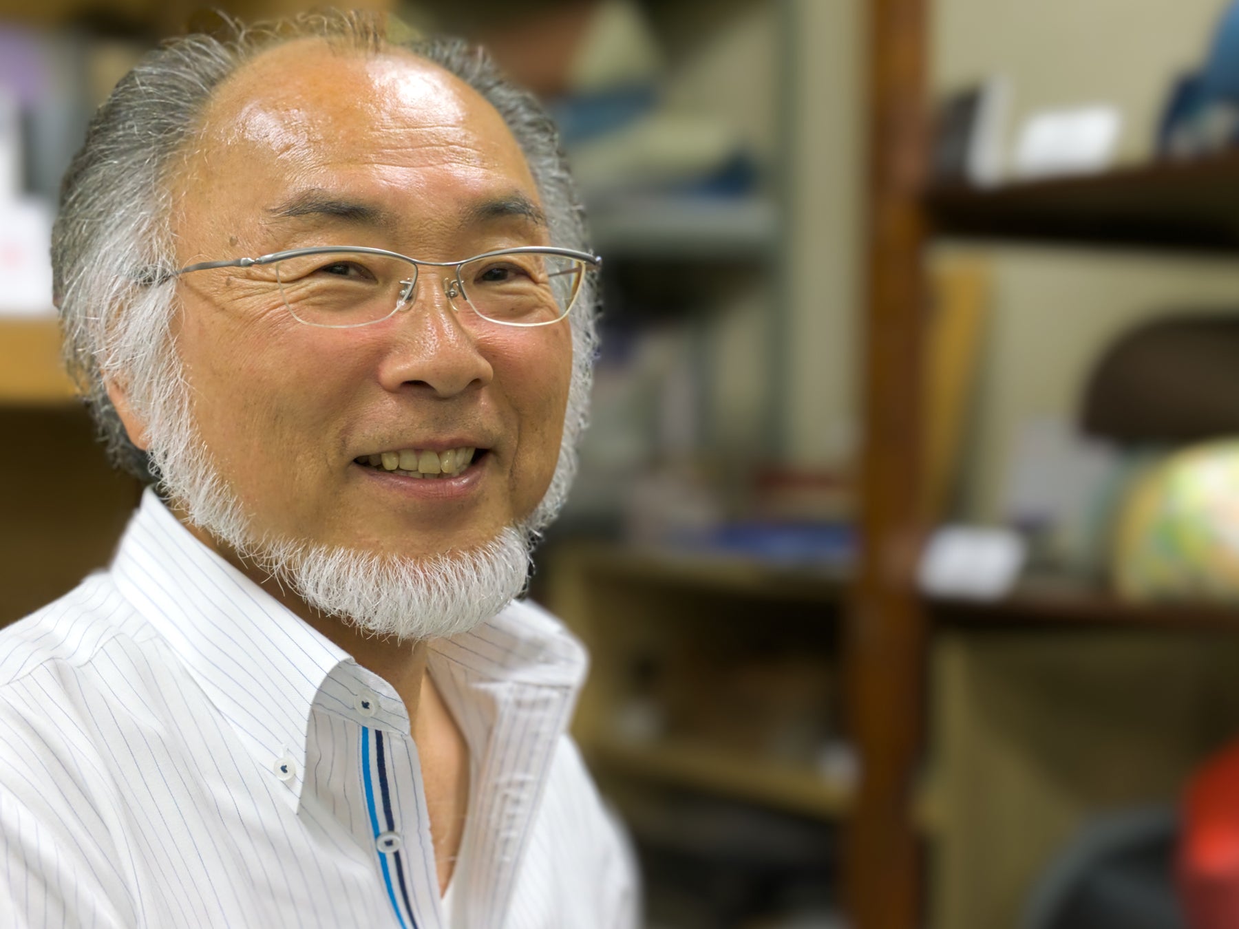 Koichiro Takaoka, owner of Takaokaya, wears a white dress shirt and glasses inside his production facility. 