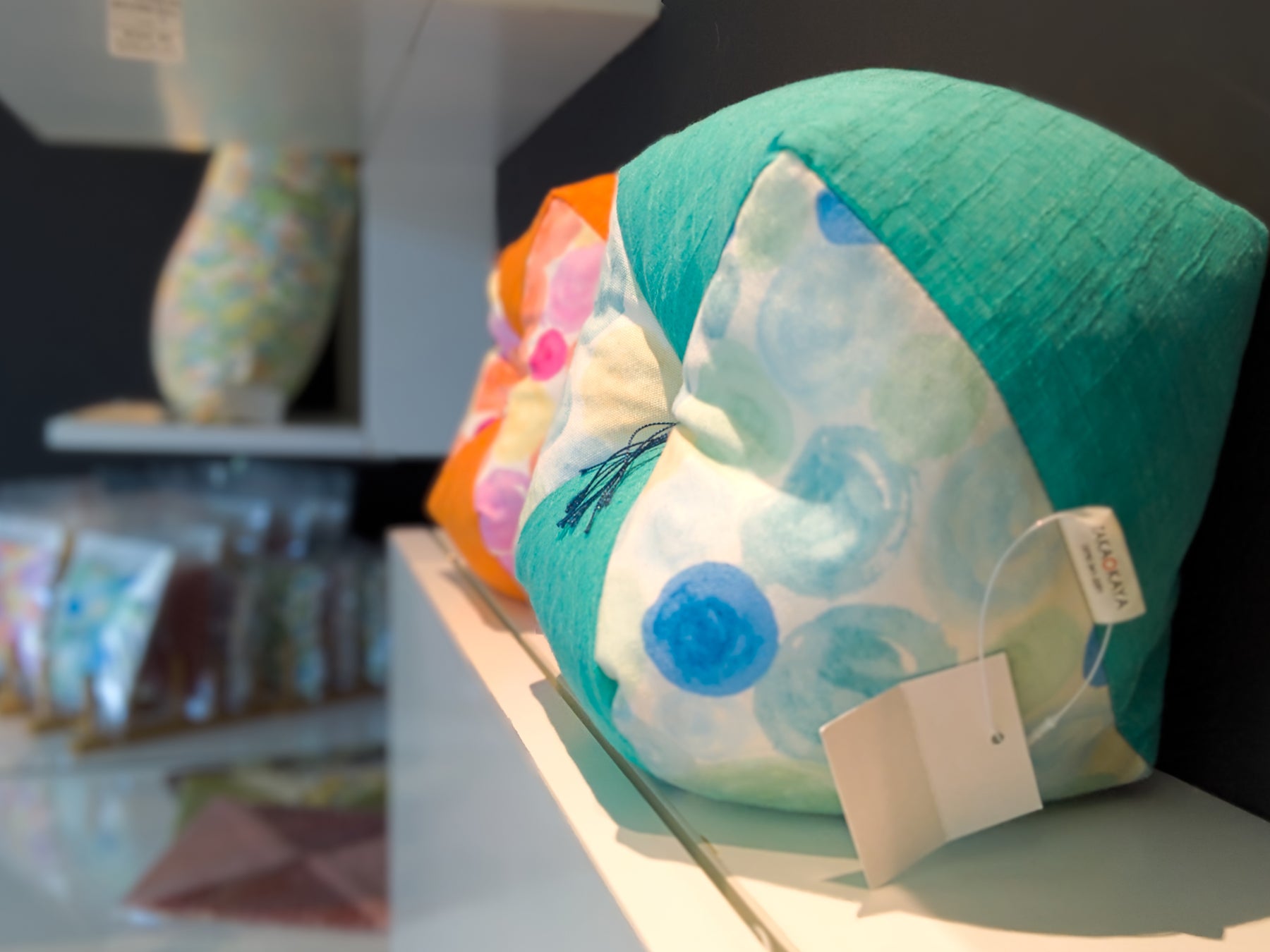 A bright green ojami cushion sectioned with white, blue, and green patterns is displayed on a shelf within Takaokaya’s flagship store. 