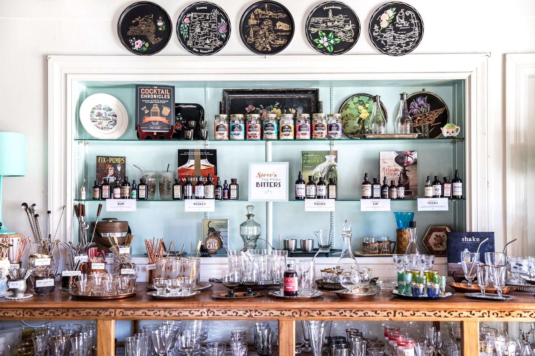 Wide shot of a retail display featuring shelves of cocktail ingredients, glassware, bar accessories, and vintage fixtures.