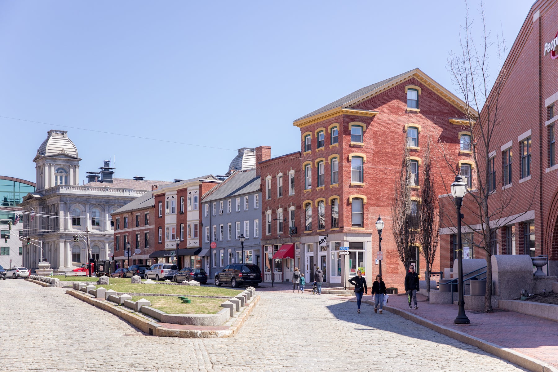 A wide shot of a cobblestone street, a row of brick buildings, and a wide grassy median in Portland, Maine.