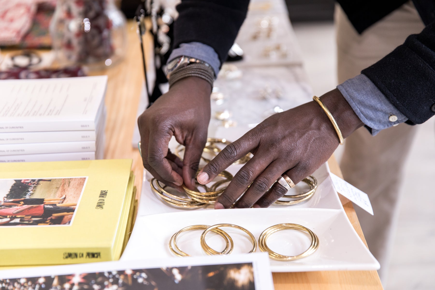 Detail of a man’s hands arranging gold bracelets on a table in a retail display.