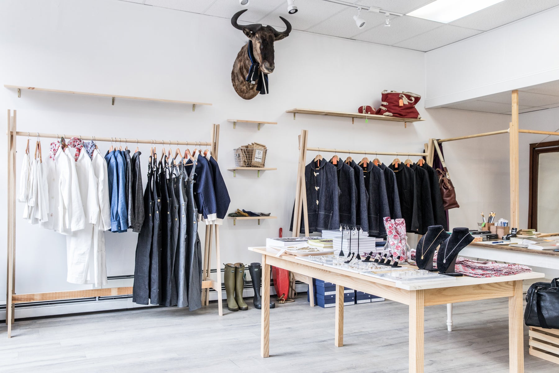 Wide shot of an airy, minimal retail store with pine fixtures, taxidermy decor, and racks of hanging denim and white garments.