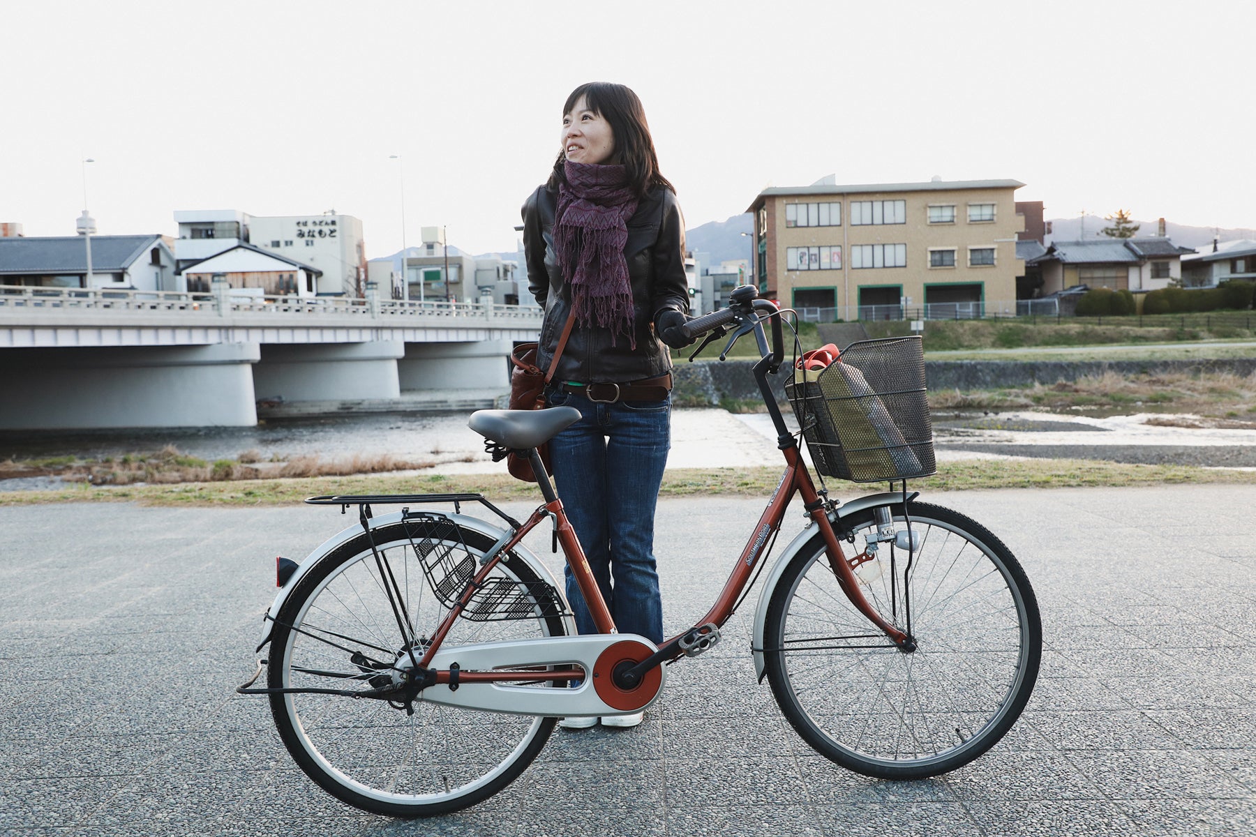 Ayumi Nicholas, in black jacket, jeans, and purple scarf, poses with her bicycle on one of her fabric sourcing trips to vintage shops. 