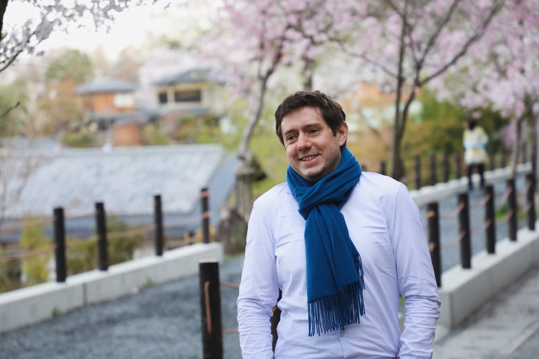 Thomas Bertrand, owner of Bento&Co, poses in white shirt and blue scarf, at one his favorite bento picnic spots, next to the river and near cherry blossoms. 