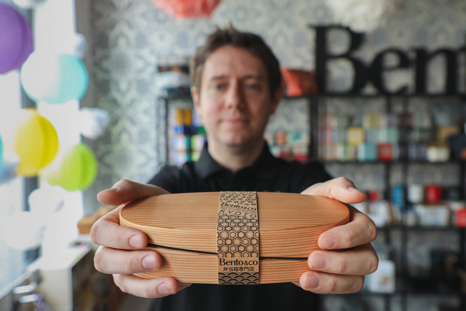 Thomas Bertrand, in a black dress shirt, holds out a bento box made from Japanese cedar. 