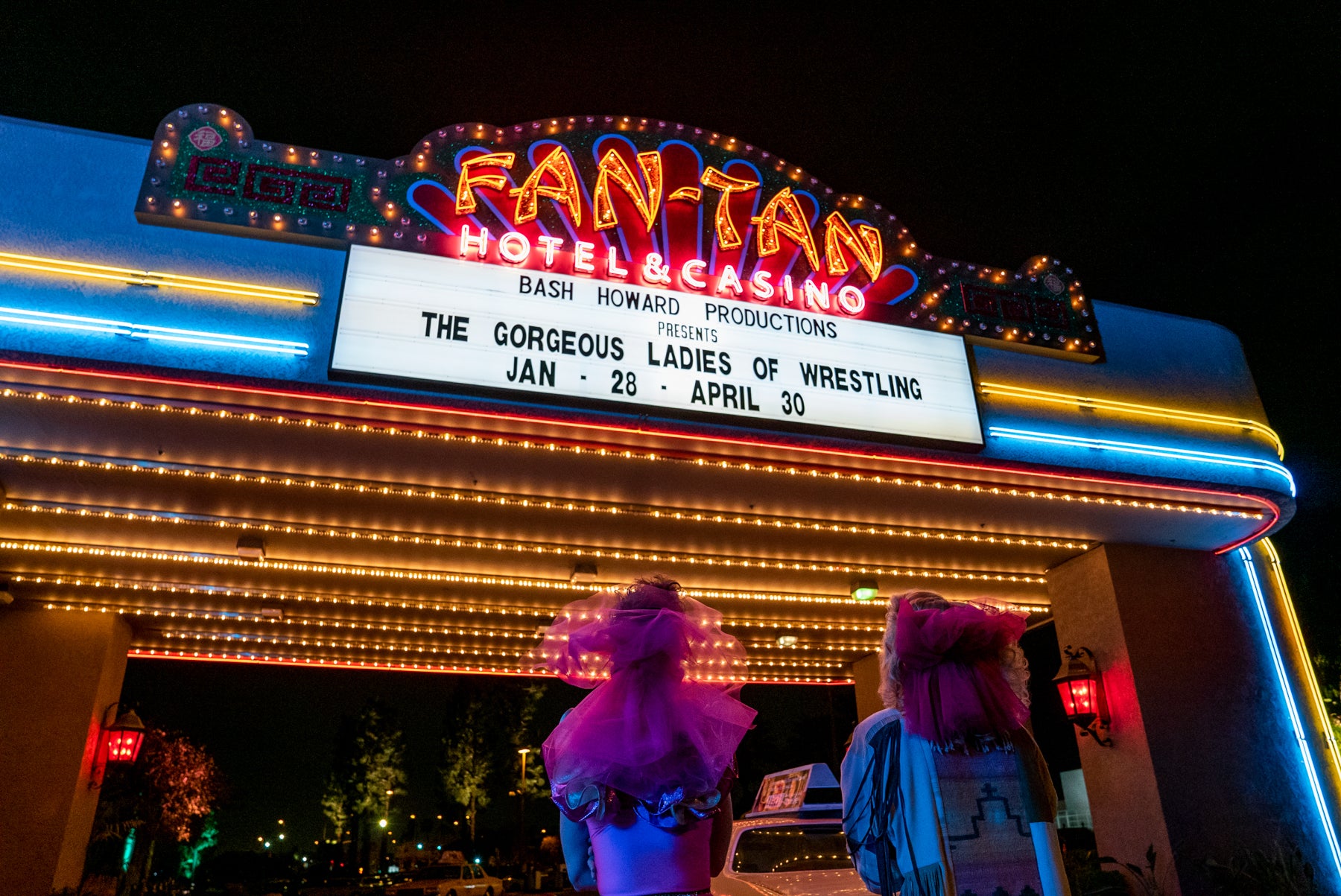 Two characters from GLOW look up at the marquee above the Fan-Tan Hotel & Casino that reads “Bash Howard Productions Presents The Gorgeous Ladies of Wrestling, Jan 28-April 30.”