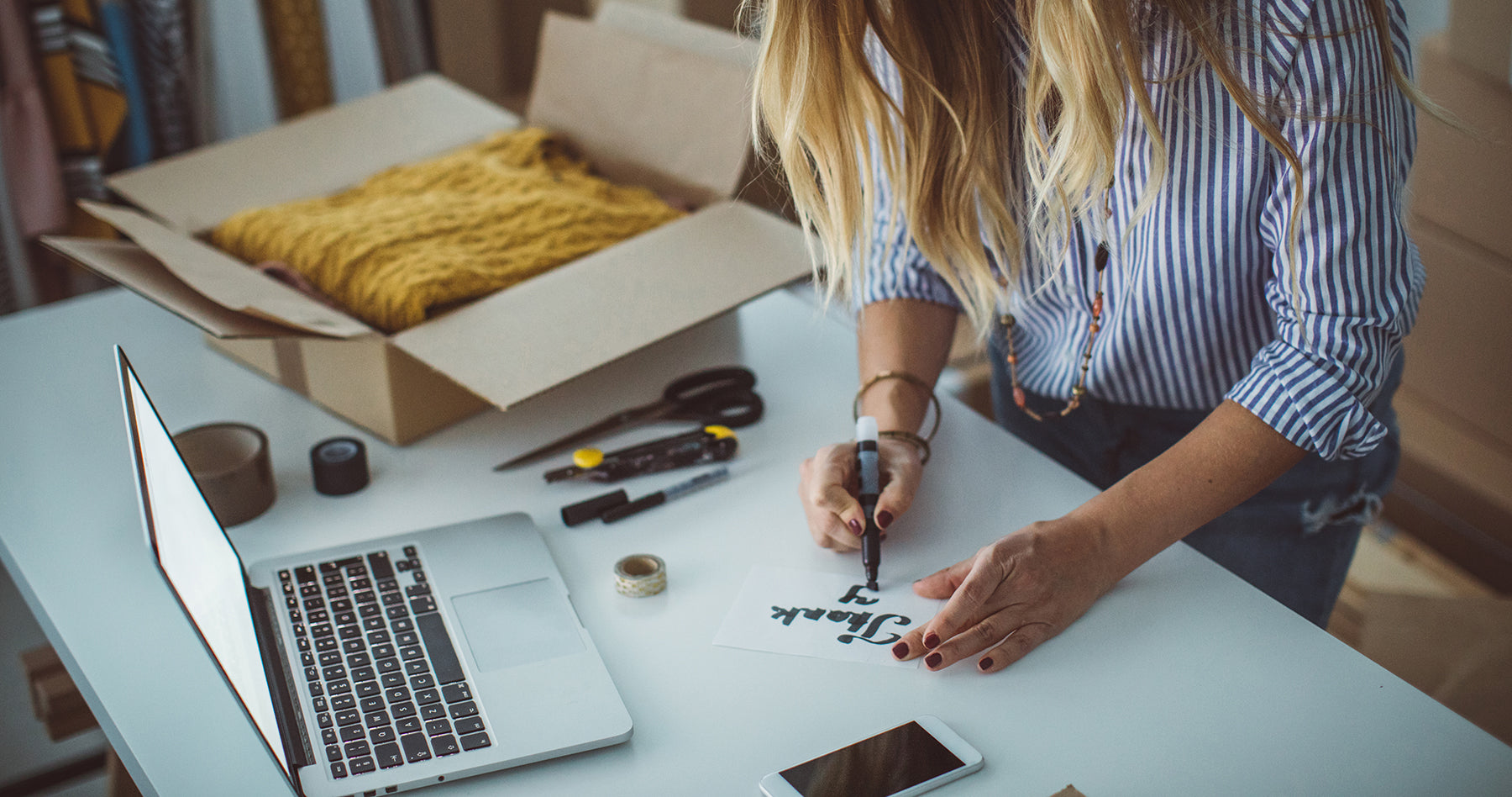 Storeowner packaging a sweater for shipping and including a thank you note in box.