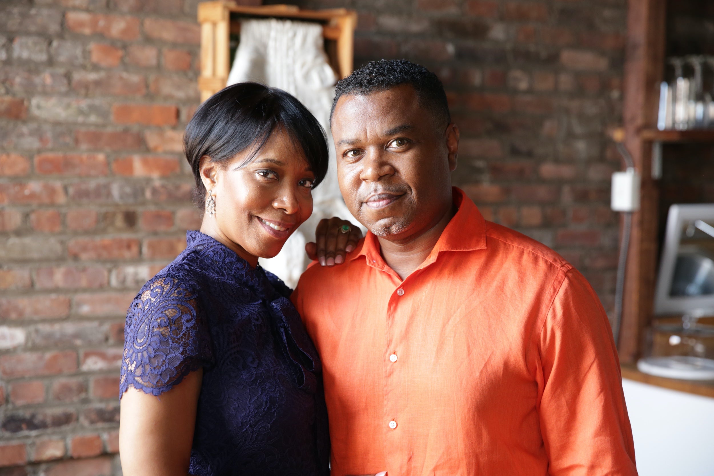 A couple stands together against a brick wall