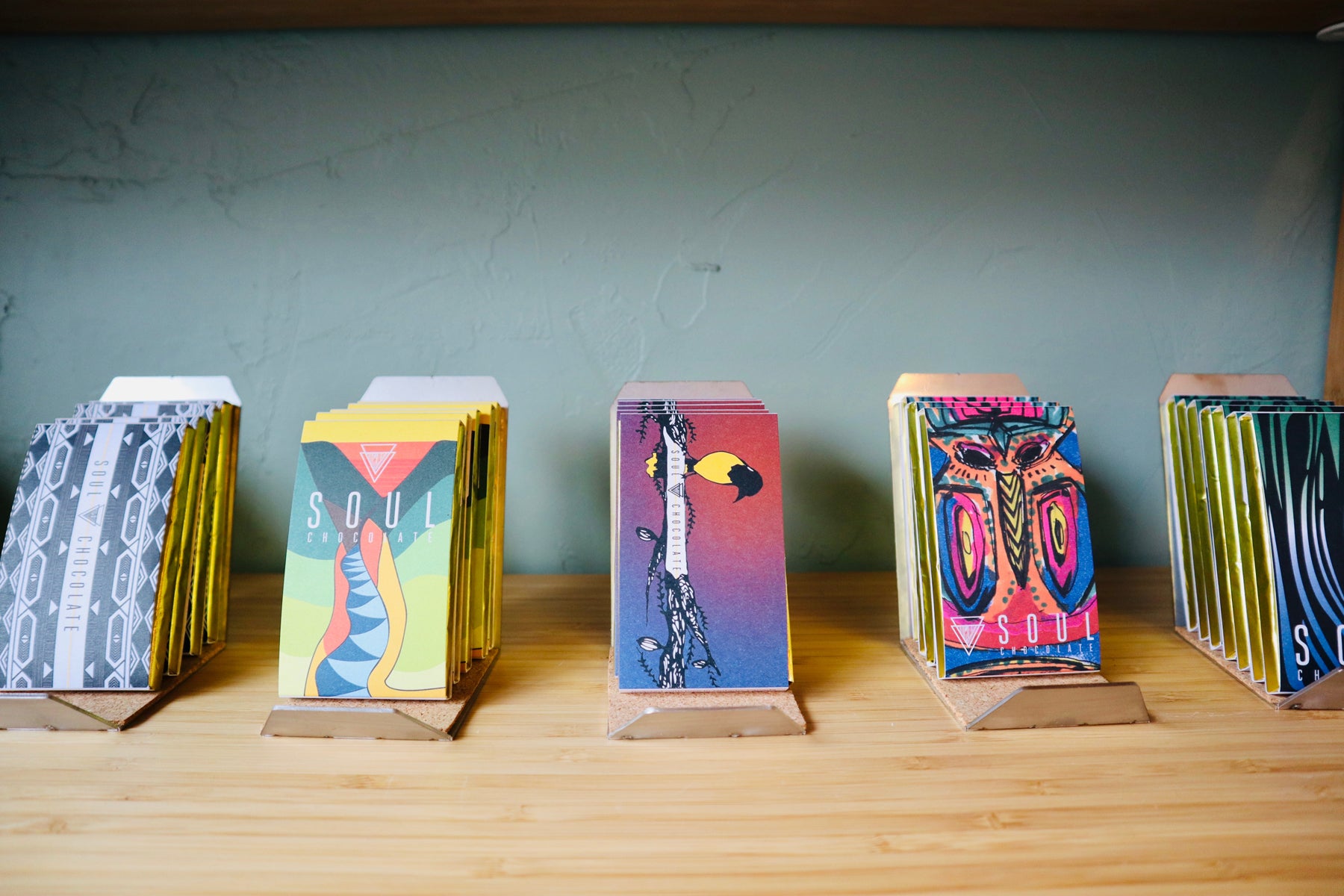 An array of chocolate bars made by Soul Roasters sit on display on a wooden shelf within their retail location. 