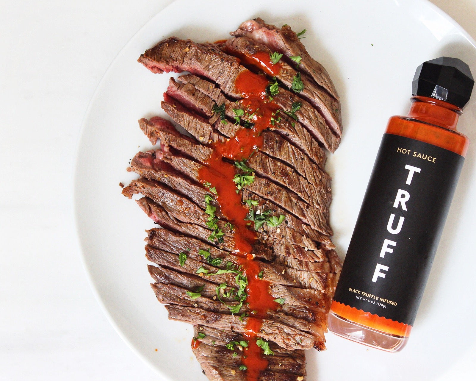 A plate of steak with a bottle of Truff sauce on the side. 