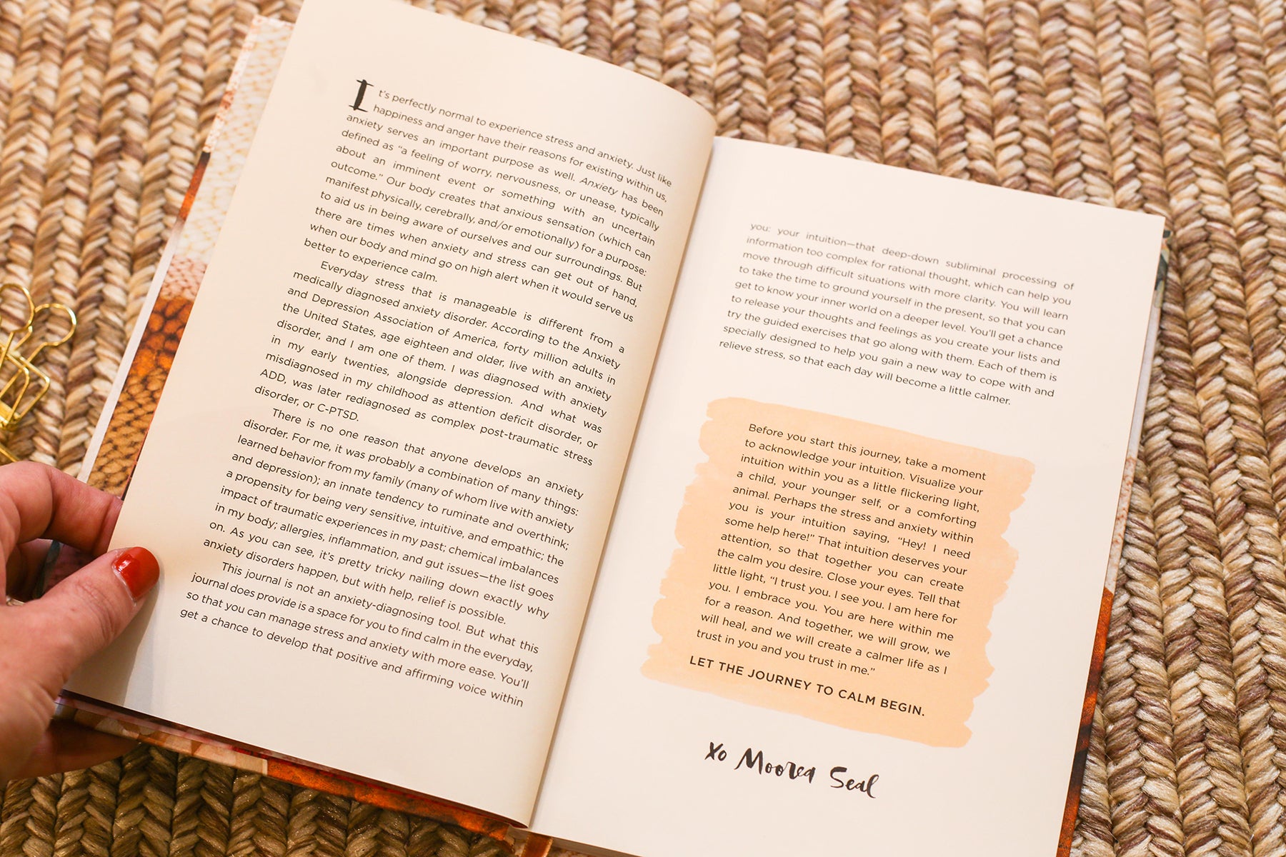 A photo of an open book held by a hand on a jute rug