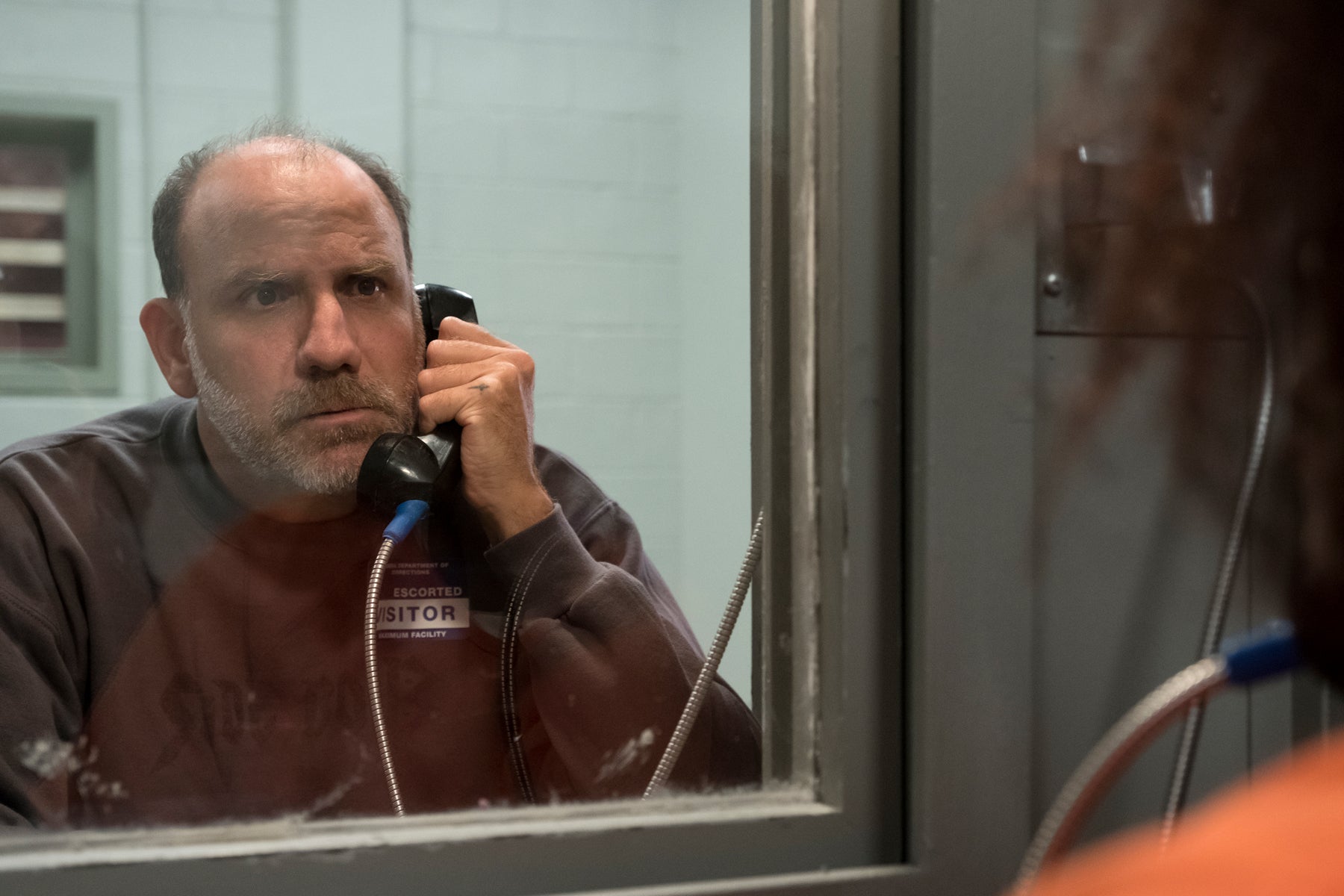 Joe Caputo speaks on a prison phone in a visitor booth in an episode of Orange Is the New Black.