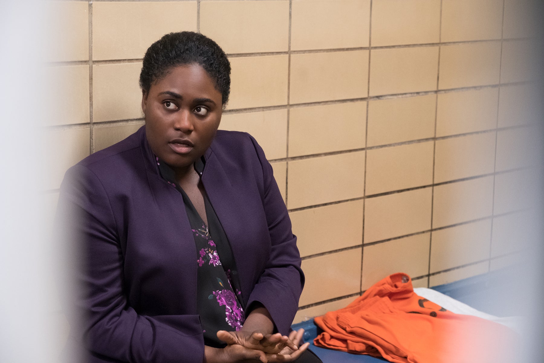 Taystee Jefferson, seen through prison bars, wears a blouse and jacket and speaks to someone off camera in an episode of Orange Is the New Black.
