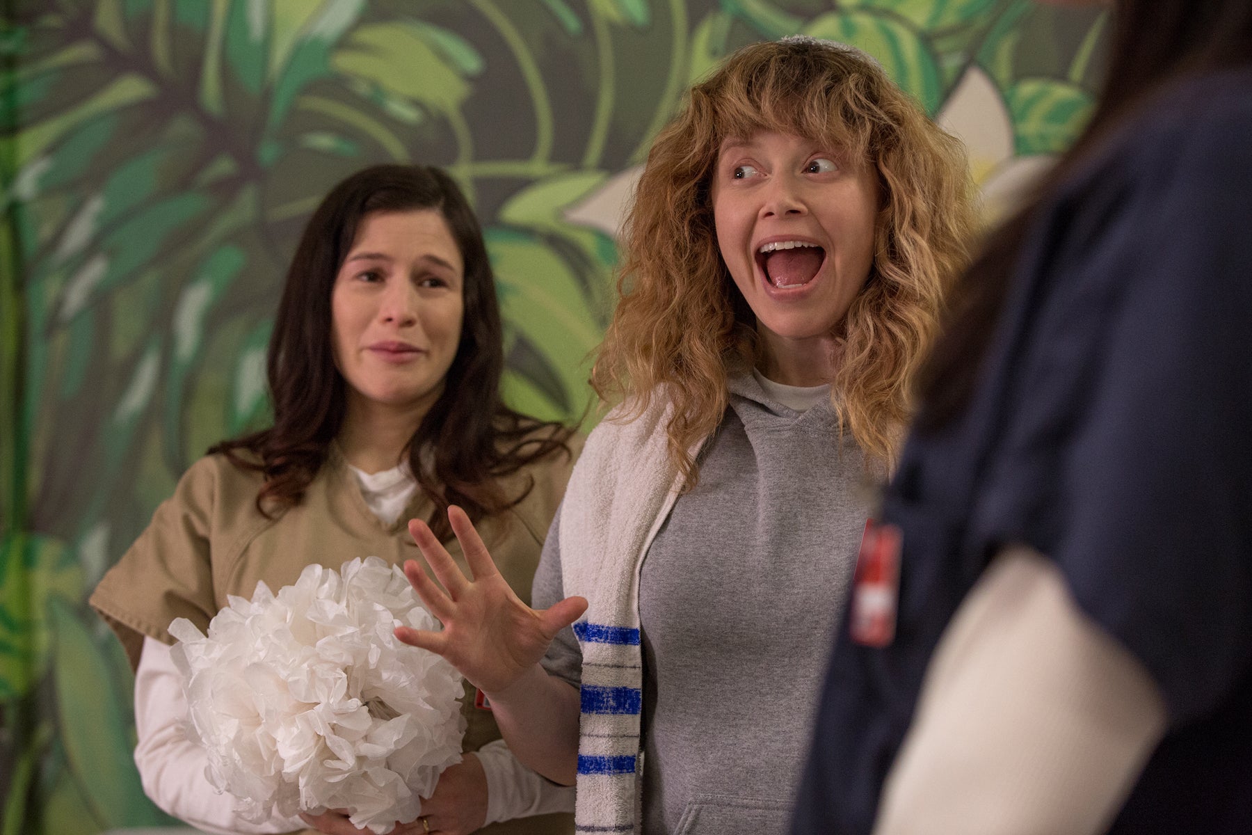 Nicky Nicholson cheers while Lorna Morello holds flowers and cries in the background in an episode of Orange Is the New Black.