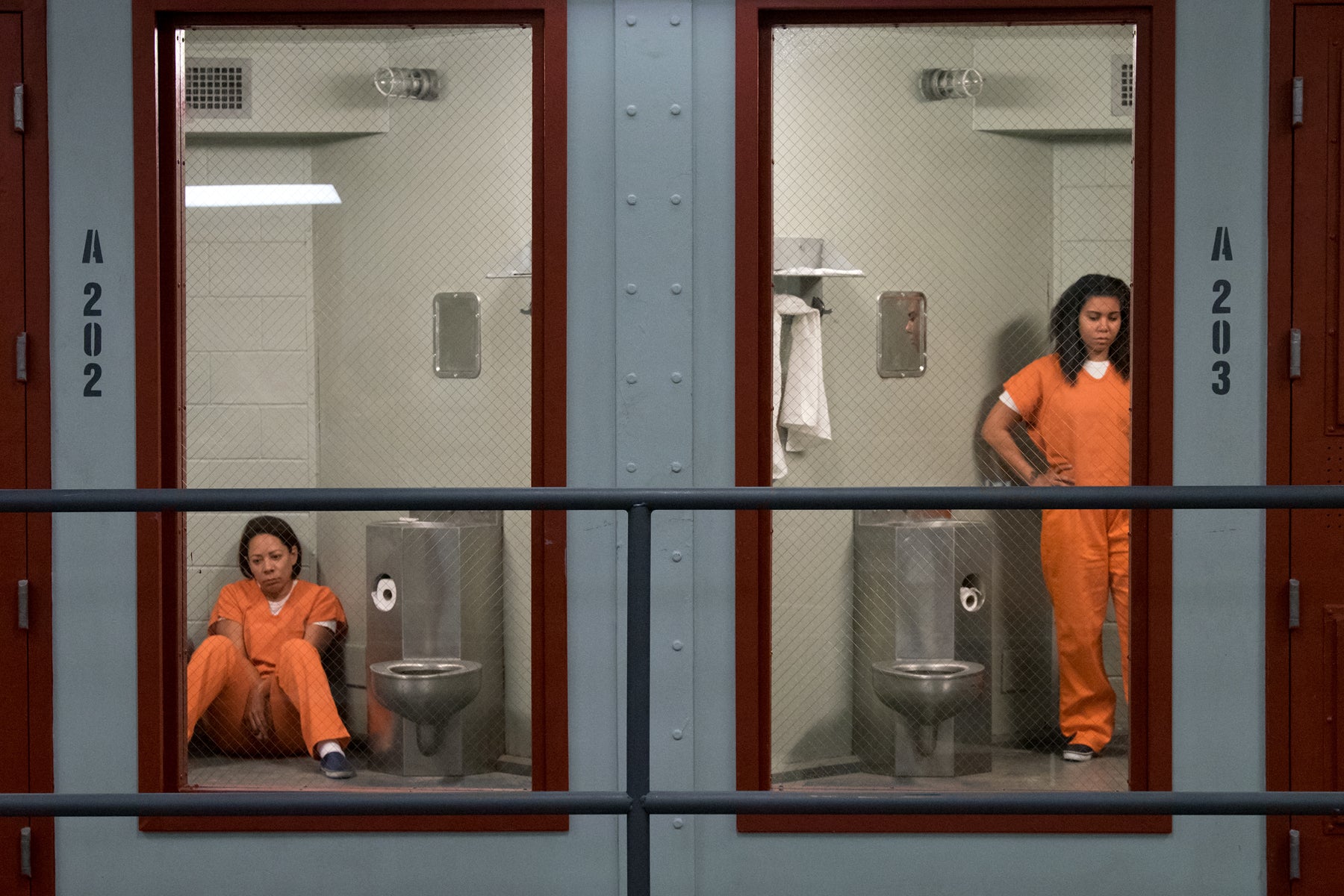 Gloria Mendoza and Maria Ruiz, looking sullen, occupy side-by-side prison cells in an episode of Orange Is the New Black.