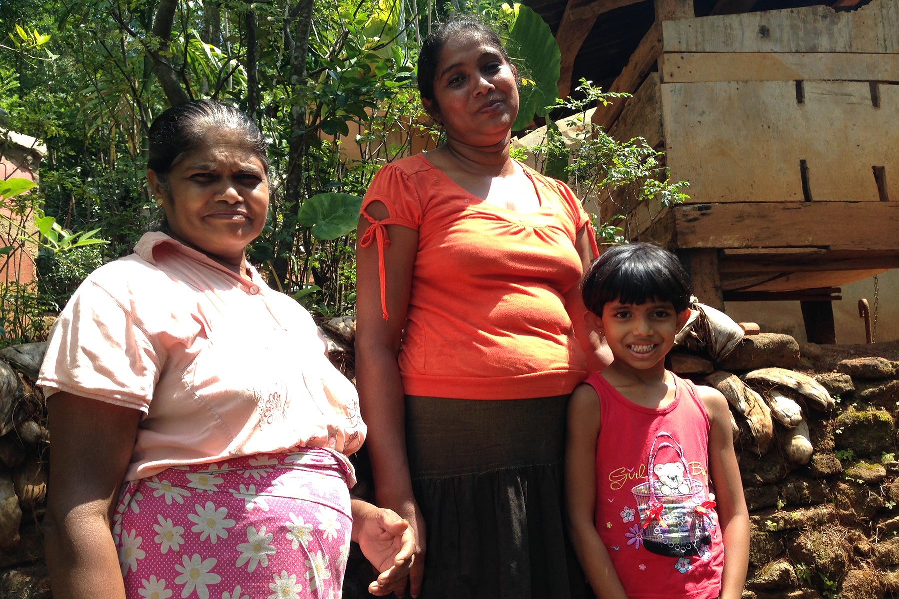 Photograph of two female organic farmers in Sri Lanka standing with a young girl between 7 and 9 years old. 