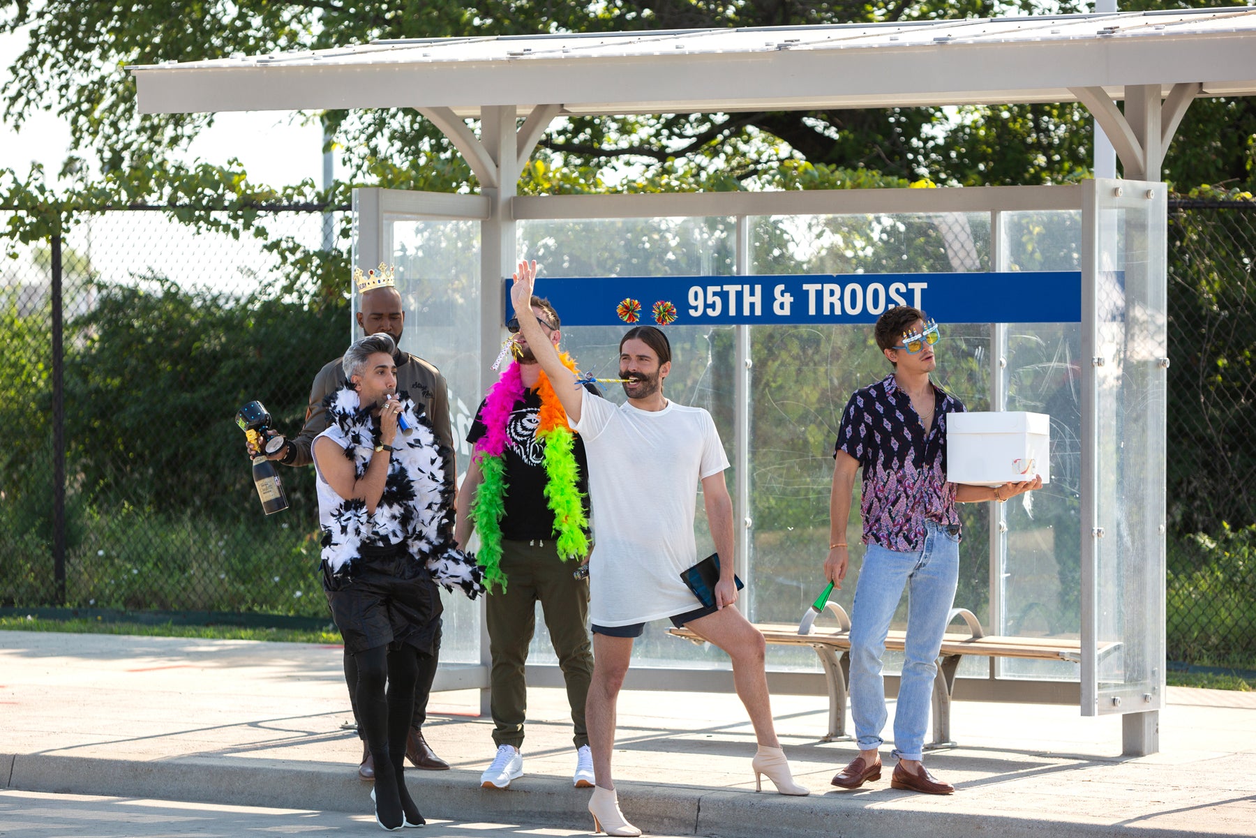 Karamo, Tan, Bobby, Jonathan, and Antoni wear party accessories and stand at a bus stop with a sign that says “95th & Troost” in an episode of Queer Eye.