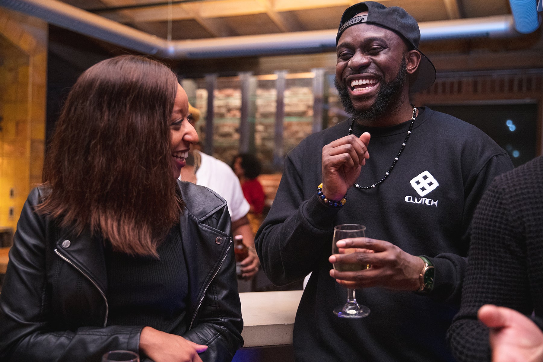 A woman in a leather jacket laughs with a man holding a wine glass at an event at AfroTech 2019. 