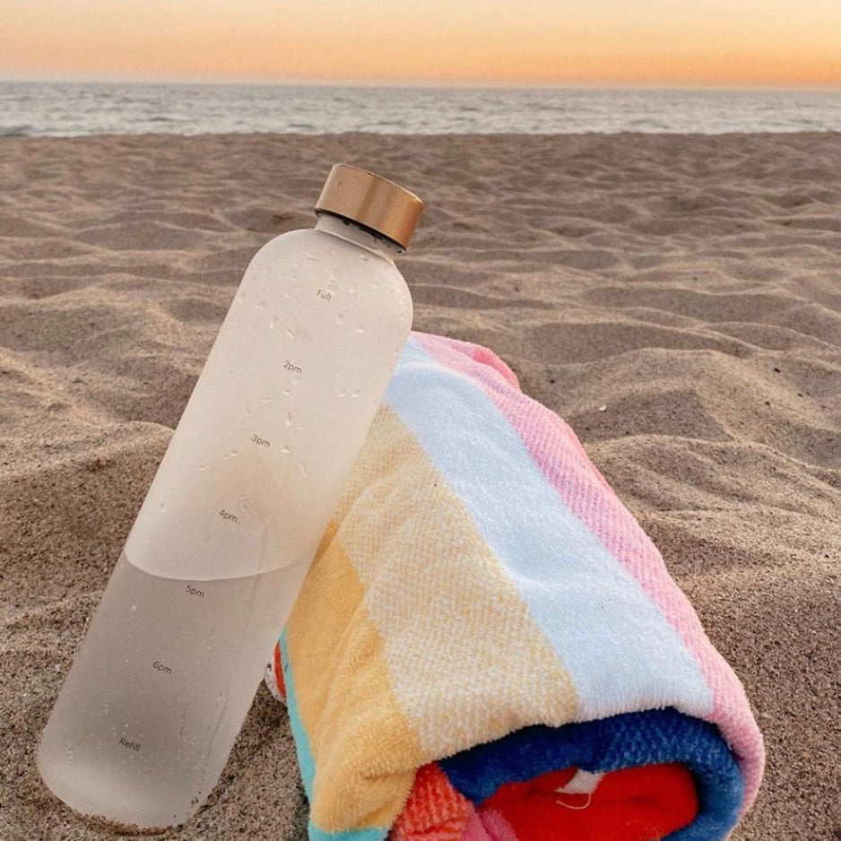 A water bottle by Healthish on the beach next to a beach towel.
