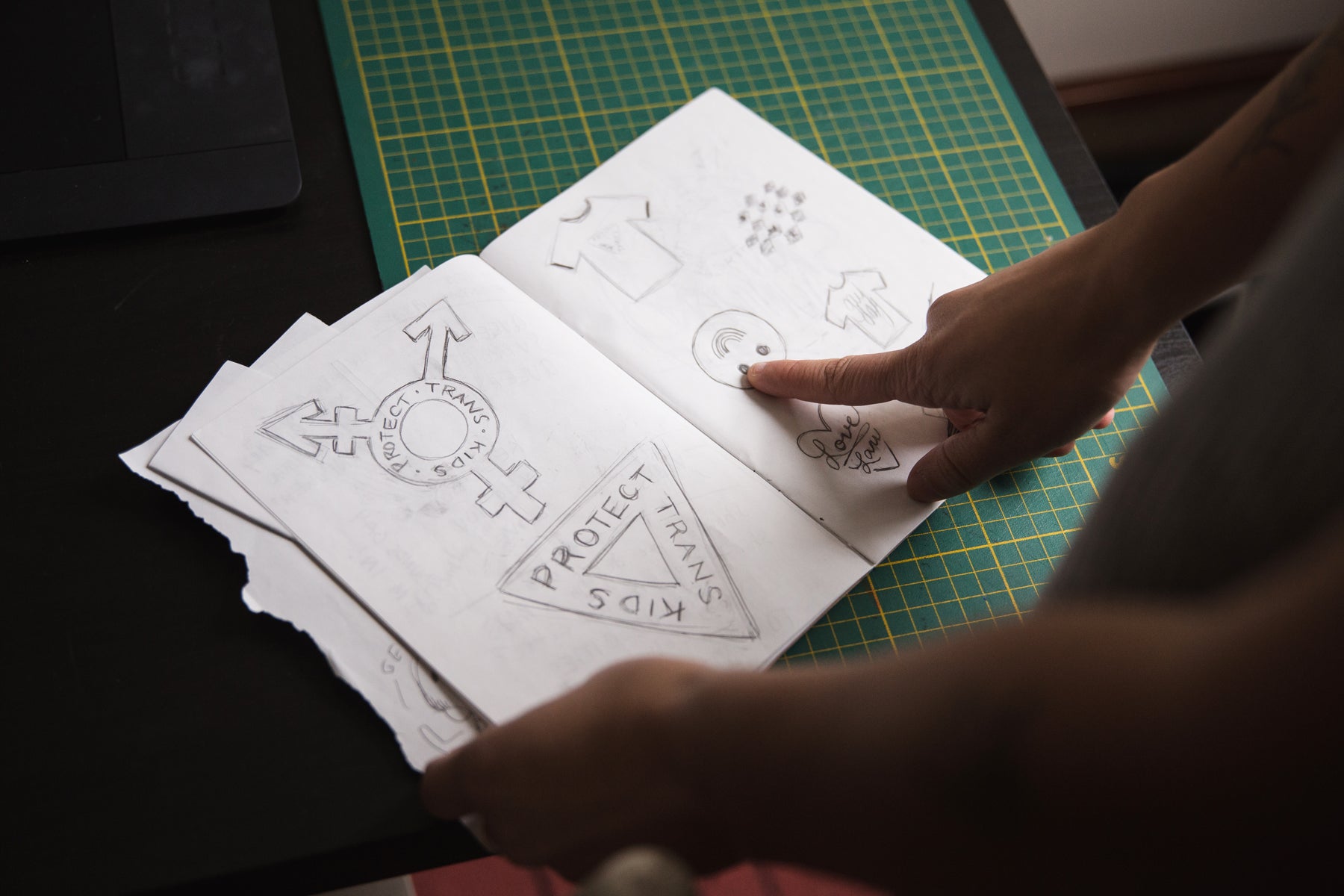 Image of designer Liz Bertorelli's sketch book with four ideas for t shirt designs drawn in pencil. 
