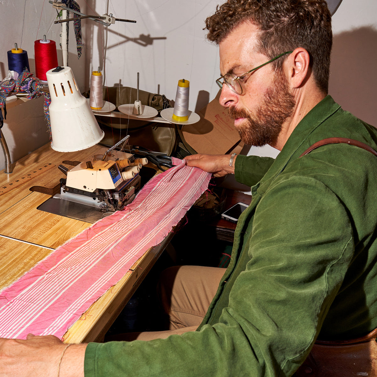 Matthew Schildkretr, founder of Late Sunday Afternoon in Venice, California, sitting at his workbench with a strip of pink fabric.