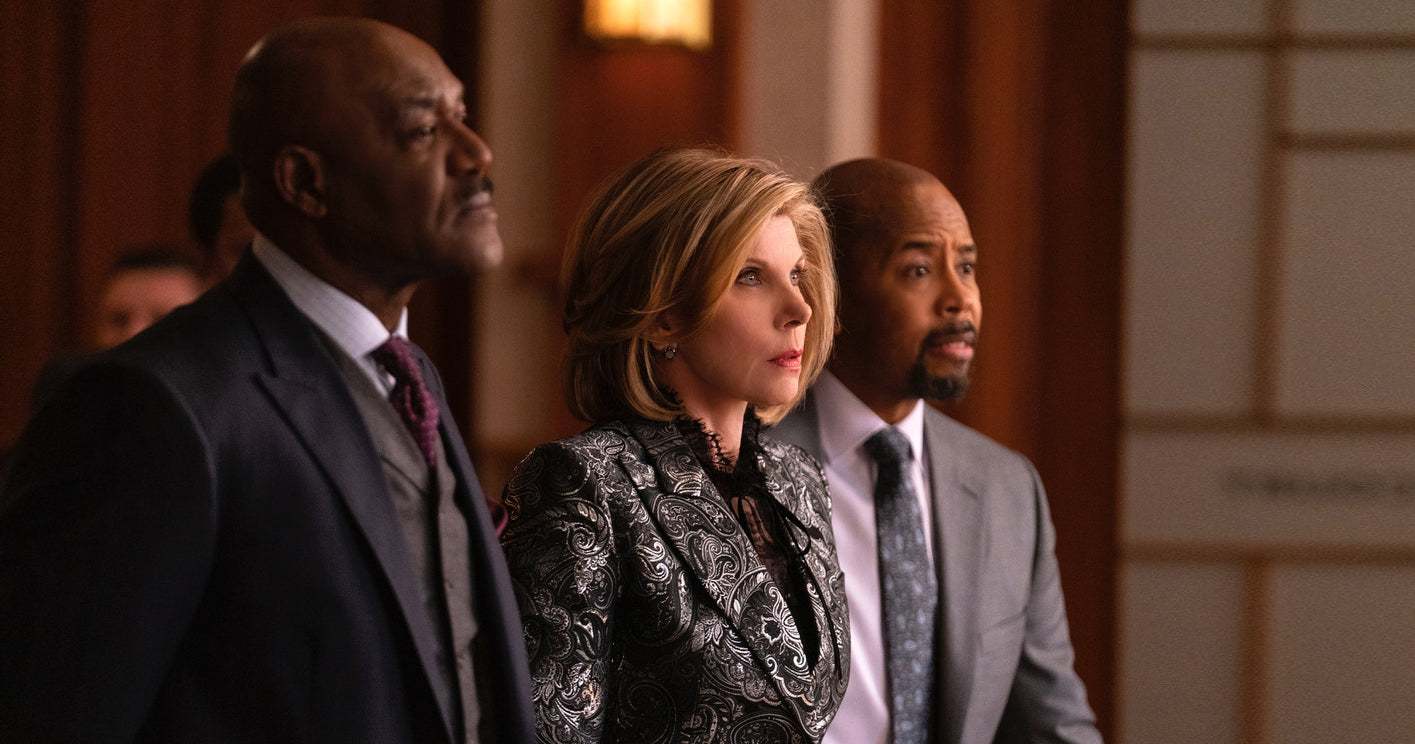 Christine Baranski from The Good Fight standing in a courtroom with a worried look on her face while two male lawyers stand on either side of her.