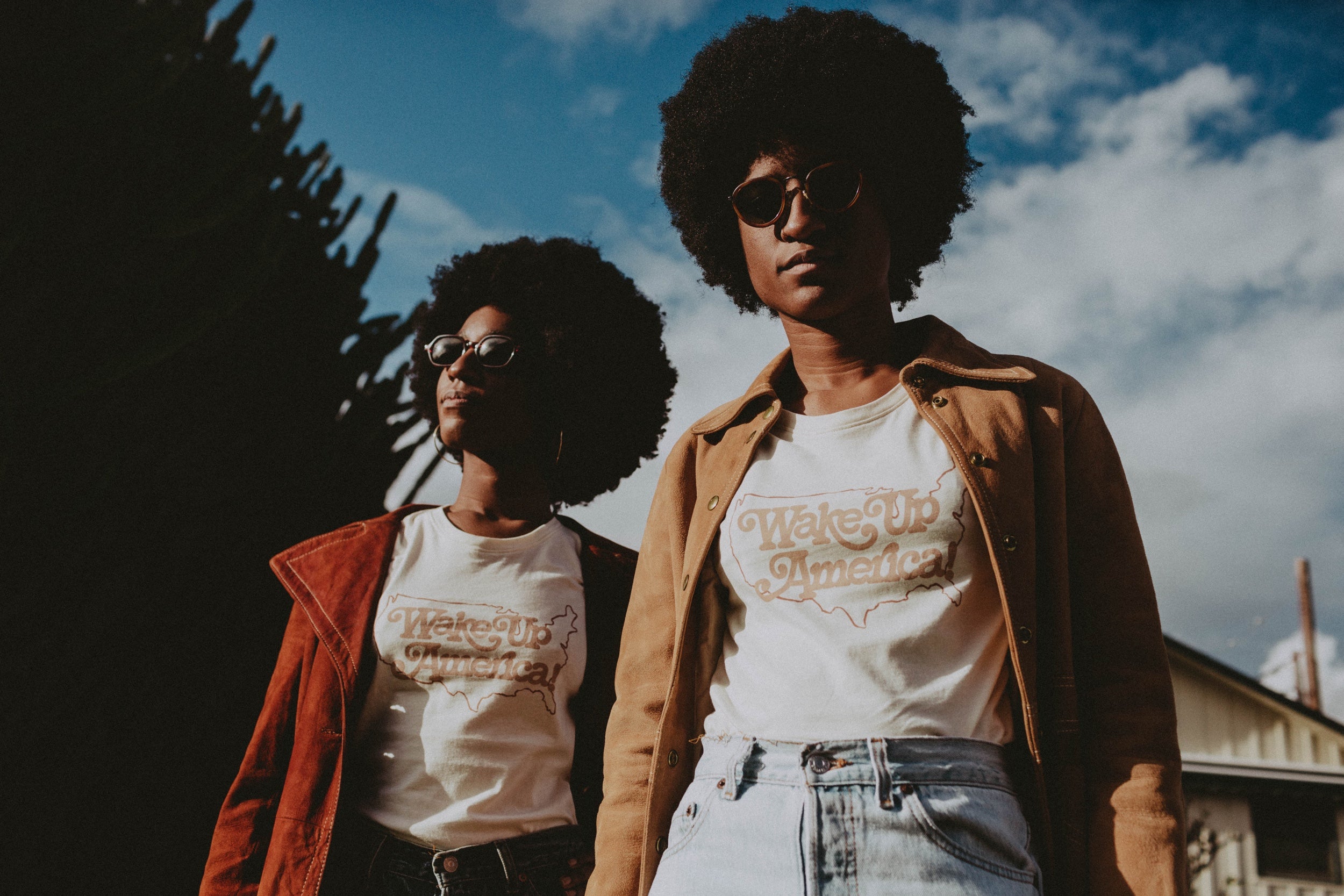 Image of a two models wearing coats and sunglasses against a sky background