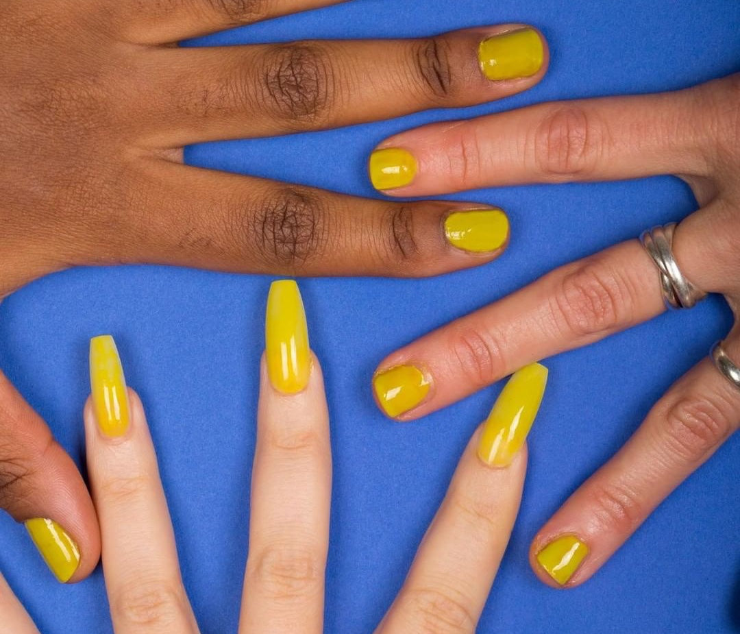 Fluide yellow nail polish modelled on 3 hands against a blue background