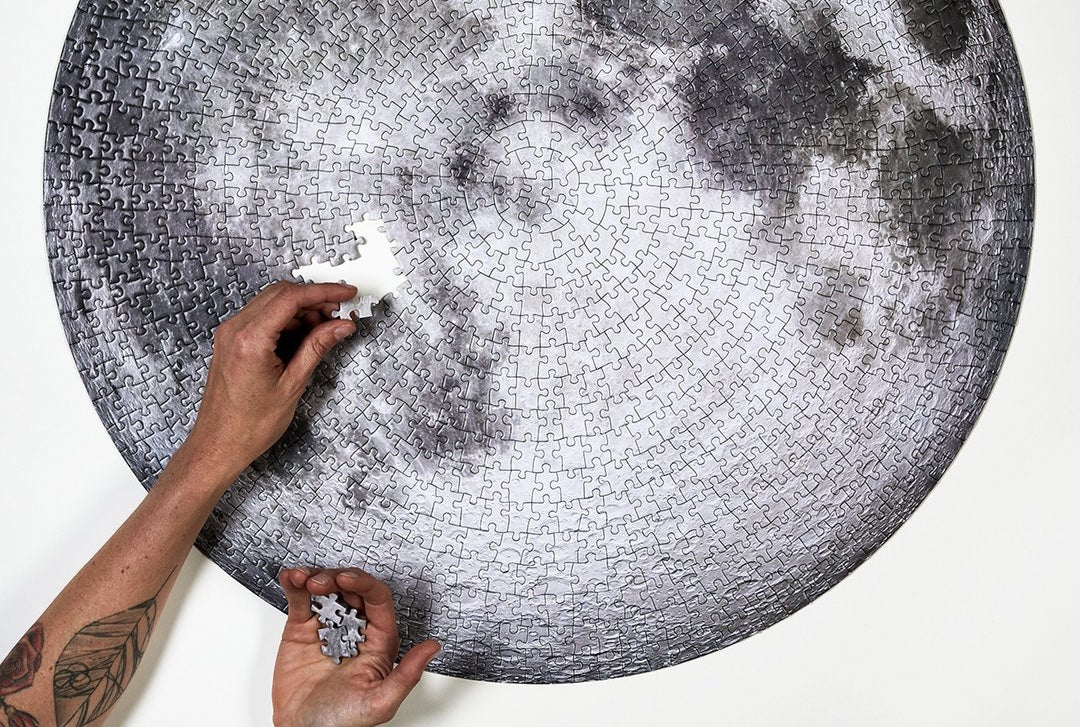 person's hands completing a puzzle of the moon