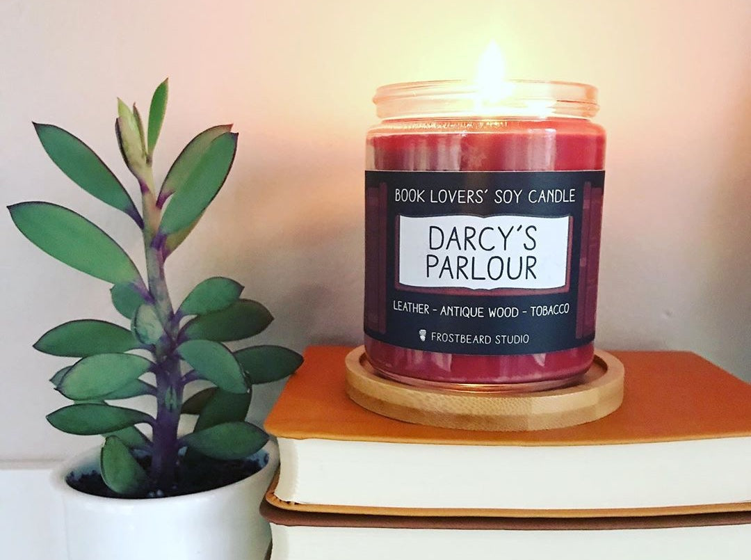 Frostbeard Studio book lover's candle in "Darcy's Parlour" fragrance, perched on books next to a succulent