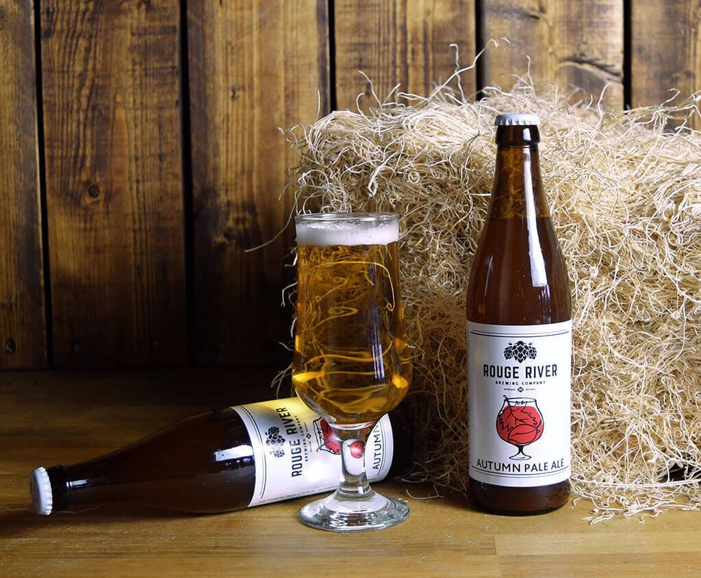 Beer bottles and a beer glass against background with wood and hay