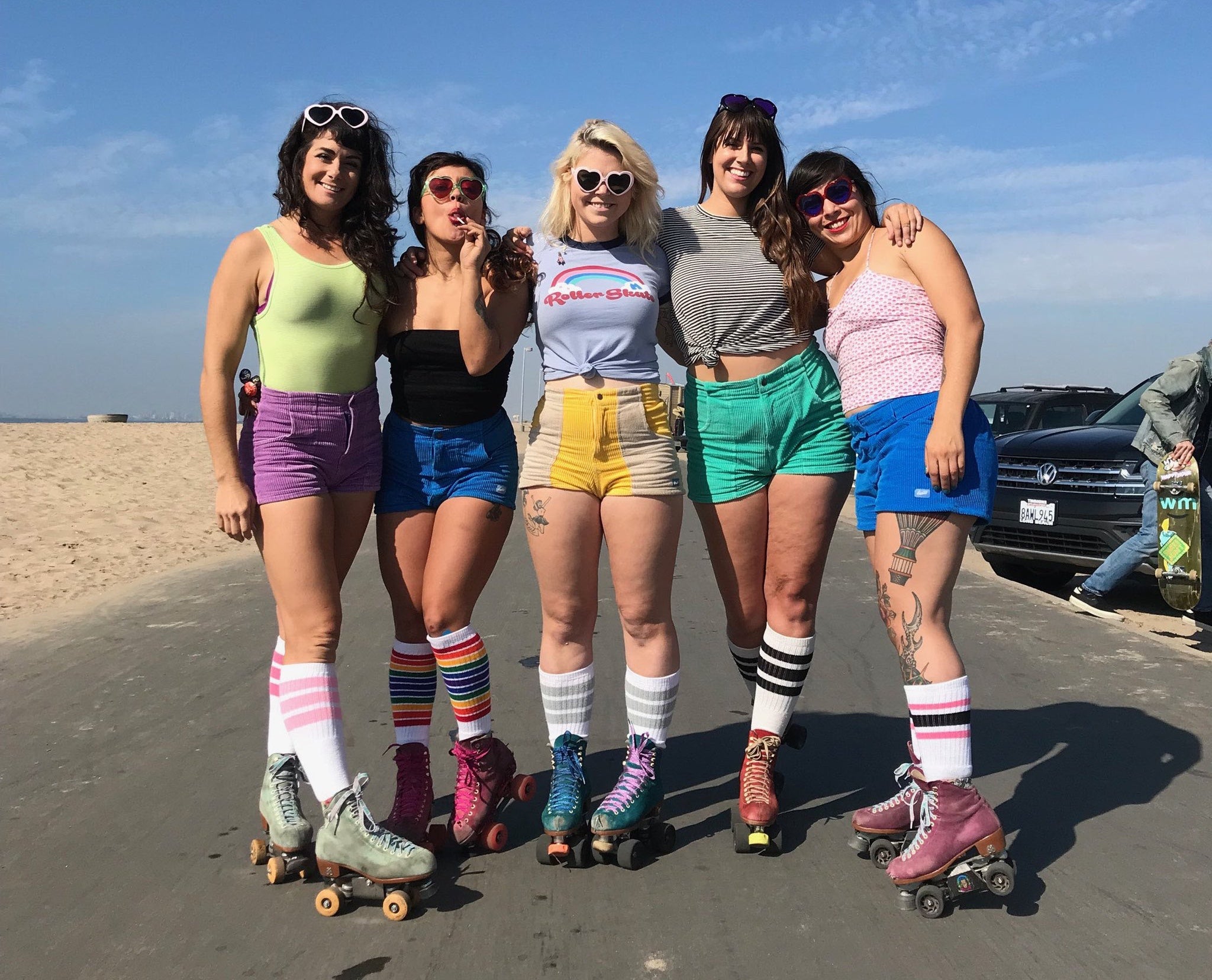 Portrait of five women wearing shorts and multi-colored roller skates on a beach path 
