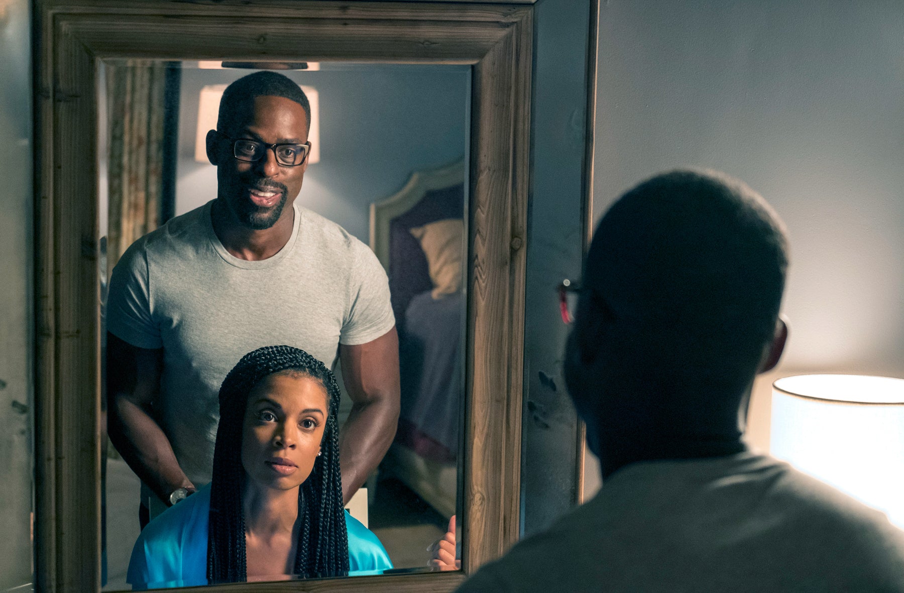 Randall Pearson (Sterling K. Brown) stands behind Beth Pearson (Susan Kelechi Watson) who sits in front of a mirror in an episode of This Is Us.