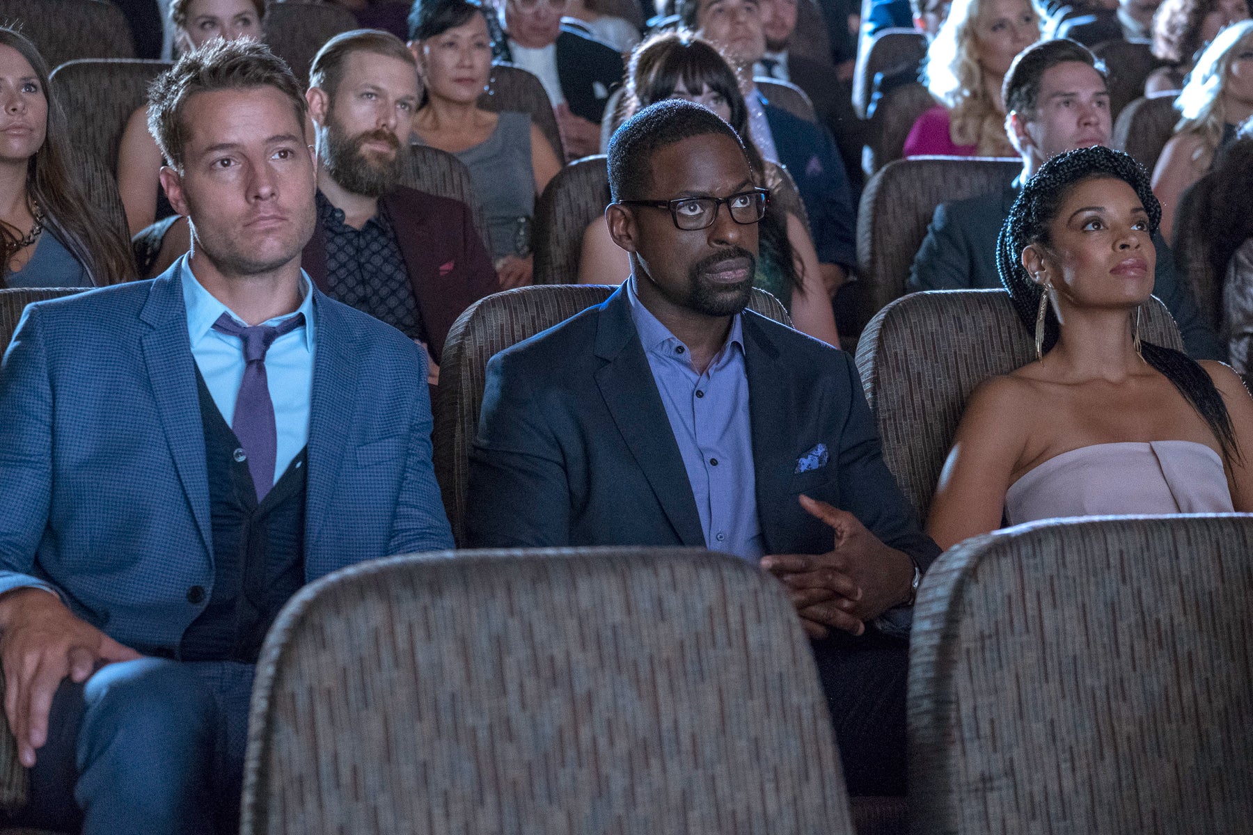 Kevin (Justin Hartley), Randall (Sterling K. Brown), and Beth Pearson (Susan Kelechi Watson) sit in a dark, crowded theater in an episode of This Is Us.